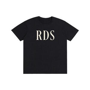 Może przedstawiać: Czarny t-shirt z krótkim rękawem z literami RDS nadrukowanymi dużą czcionką szeryfową w kolorze złamanej bieli na środku klatki piersiowej. Odzież posiada standardowy okrągły dekolt i proste wykończenie dołu, prezentując prosty i czysty design.