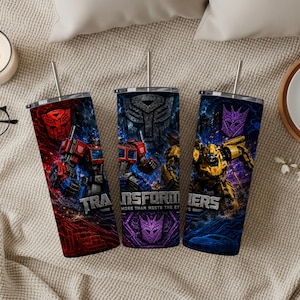 May include: Three cylindrical metal tumblers with lids and straws, each featuring Transformers graphics. The designs include Optimus Prime in red and blue, Bumblebee in yellow, and various Autobot and Decepticon logos against dark, cosmic backgrounds.