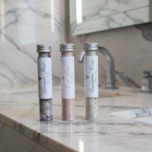 以下が含まれることがあります： 銀色のキャップが付いた3本のガラスチューブ。それぞれにバスソルトが入っています。「Lavender Reset」、「Core Blush」、「Eucalyptus Clear」とラベルが貼られています。ラベルには植物のイラストが描かれています。