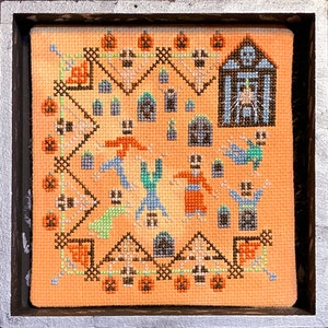 May include: A cross-stitch pattern featuring a spooky Halloween scene with skeletons, pumpkins, and a haunted house. The design is stitched on a light orange fabric with black, white, green, and blue thread.