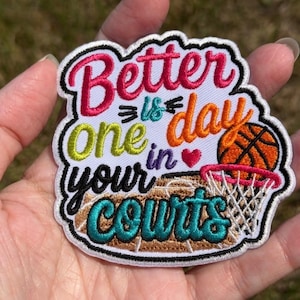 May include: An embroidered patch with a white background featuring the text Better is one day in your courts in pink, teal, lime green, orange, and black thread. A small red heart and an orange basketball with a white net are included.