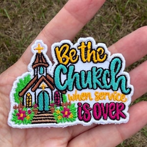 May include: An embroidered patch featuring a church building with a brown roof, teal doors, and yellow accents. The text reads "Be the Church when service is over" in yellow, teal, and pink thread. The design includes green foliage and pink flowers.