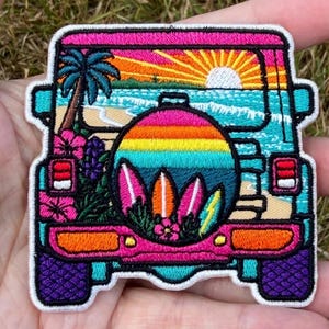 Puede incluir: Un parche bordado rectangular que muestra la vista trasera de un vehículo con una cubierta para la rueda de repuesto. El diseño representa una escena de playa tropical con atardecer, palmera, flores de hibisco y tres tablas de surf.