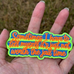 May include: An embroidered patch with a neon green border and horizontal stripes of neon green and blue. The text "Sometimes I have to tell myself it's just not worth the jail time" is stitched in orange thread across the centre of the patch.