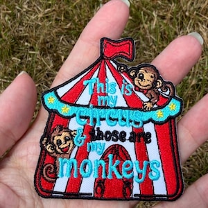 May include: An embroidered patch shaped like a red and white striped circus tent with a red flag on top. Two brown monkeys are featured on the tent. The text reads: This is my circus & those are my monkeys in bright blue and black thread.