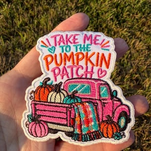 May include: An embroidered patch featuring a pink truck carrying pumpkins and a plaid blanket. The text reads TAKE ME TO THE PUMPKIN PATCH in pink and orange thread. The design includes small hearts and teal accents on a white fabric background.