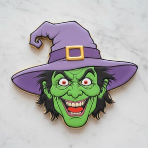 Puede incluir: Una galleta con forma de cara de bruja, con piel verde brillante, cabello negro desordenado y una amplia sonrisa con dientes. La bruja lleva un sombrero morado grande y puntiagudo con una hebilla dorada. Los ojos son rojos con pupilas negras.