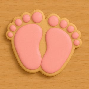 Puede incluir: Una galleta con forma de pie de bebé, con una base marrón claro y glaseado rosa. La galleta presenta dos pies con dedos redondeados, ideal para un baby shower o una revelación de género. La galleta está sobre una superficie de madera marrón claro.