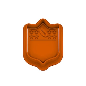 May include: An orange cookie cutter in the shape of the NFL shield. The shield features a football and stars. The cutter is made of plastic and is designed for making cookies or other treats.