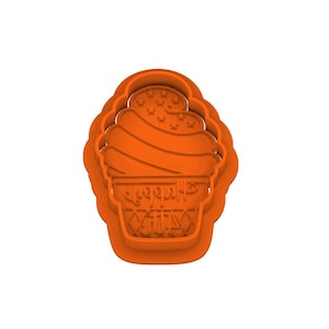 May include: An orange plastic cupcake-shaped cookie cutter featuring a swirled frosting top with embossed star details and a base with the text Happy Birthday in a script font, surrounded by a diamond pattern border on the lower section.