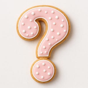 May include: A question mark-shaped cookie with a pink frosted surface and white polka dots. The cookie has a light brown, baked appearance with a white border around the pink frosting. The cookie is a sweet treat.