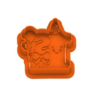 Puede incluir: Cortador de galletas de plástico naranja con forma del número "21", una vela, un globo y una caja de regalo. La vela tiene una cara sonriente y una llama. Para un cumpleaños.