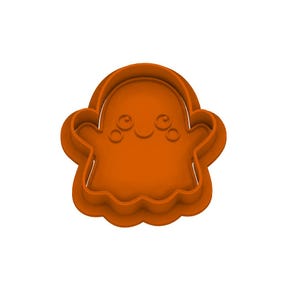 May include: An orange plastic cookie cutter shaped like a ghost with a rounded head, two outstretched arms, and a wavy bottom edge. The interior features embossed details of two circular eyes and a small curved mouth centered on the face.