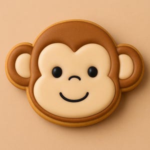 May include: A monkey-shaped cookie with a smiling face. The cookie features a light brown outline, a tan face, and dark brown details for the ears and top of the head. The eyes are black, and the mouth is a curved black line.