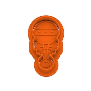 Puede incluir: Un cortador de galletas de plástico naranja con forma de sonajero para bebé. El sonajero tiene una parte superior redonda con tres círculos pequeños, un lazo y una parte inferior con un círculo pequeño.