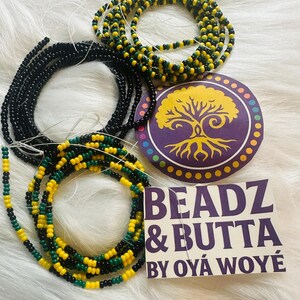 Può includere: Un assortimento di perline per la vita in nero, verde e giallo. È presente anche un disegno circolare viola e giallo con una grafica ad albero, insieme a un'etichetta bianca con la scritta "BEADZ & BUTTA BY OYÁ WOYÉ."