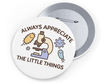 Op de afbeelding: Een witte button met de tekst "ALWAYS APPRECIATE THE LITTLE THINGS" in bruine letters. Het ontwerp bevat een cartoon microscoop, bacteriën en andere wetenschappelijke illustraties in blauw, beige en geel.