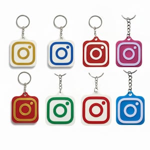 Könnte beinhalten: Acht Schlüsselanhänger mit dem Instagram-Logo in verschiedenen Farben: Gold, Blau, Rot und Pink. Jeder Schlüsselanhänger hat eine quadratische Form mit abgerundeter Innenseite und einem silbernen Schlüsselring.