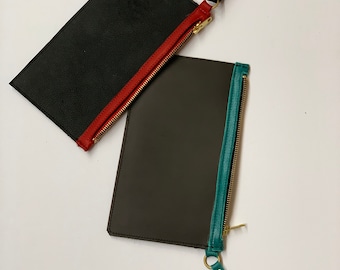 May include: Two leather zippered pouches with contrasting colored zippers and pull tabs. The top pouch is black with a red zipper and pull tab. The bottom pouch is brown with a teal zipper and pull tab.