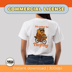 May include: White t-shirt with a raccoon graphic riding a bicycle with a basket. The raccoon wears sunglasses and a striped jacket. Text on the shirt reads "I'd rather be thrifting" in orange. The image includes the words "Commercial License" and "instant download | 300dpi".