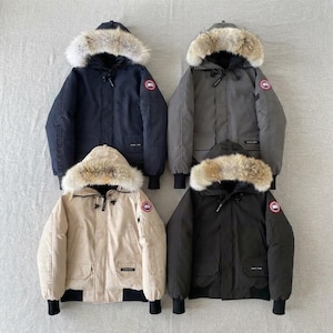 Puede incluir: Cuatro chaquetas de invierno aisladas con capuchas ribeteadas en piel, dispuestas en una cuadrícula de dos por dos. Las chaquetas son azul marino, gris carbón, beige y negro. Cada una presenta un parche circular rojo, blanco y azul en la manga.