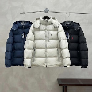 Puede incluir: Tres chaquetas acolchadas colgadas en un perchero, en colores azul marino, crema y negro. Cada chaqueta cuenta con capucha, cremallera frontal completa, dos bolsillos laterales y un pequeño bolsillo vertical con cremallera en el pecho.