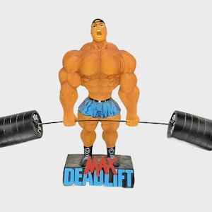 May include: A figurine of a muscular bodybuilder lifting a barbell. The figure is orange with a blue skirt and black shoes. The base reads "MAX DEADLIFT" in blue and red. The barbell has black weights.