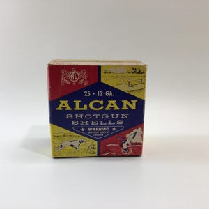 May include: A vintage box of ALCAN shotgun shells. The box is red, yellow, and blue with the text "ALCAN SHOTGUN SHELLS" in yellow. The box also has illustrations of a dog and a person shooting.