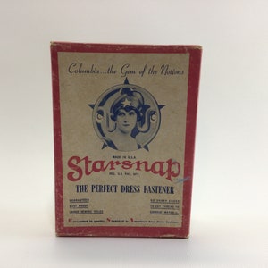 May include: A vintage box of Starsnap dress fasteners. The box is red and white with a picture of a woman in a star-shaped frame. The text on the box reads "Columbia...the Gem of the Notions" and "Starsnap - The Perfect Dress Fastener".