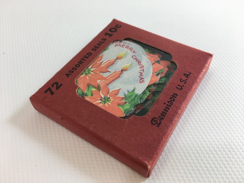 K&ouml;nnte beinhalten: Eine rote Schachtel mit 72 verschiedenen Weihnachtsaufklebern, die eine Weihnachtsstern und Kerzen mit dem Text "Merry Christmas" zeigen. Die Schachtel ist mit "72 Assorted Seals 10c Dennison U.S.A." beschriftet.