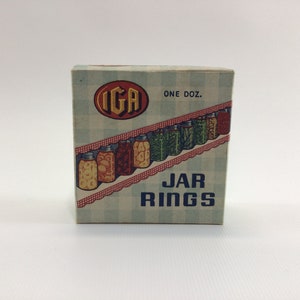 May include: A box of IGA jar rings, with a blue and white checkered background and a picture of jars of preserved food. The box says "One Doz. JAR RINGS" on the front.