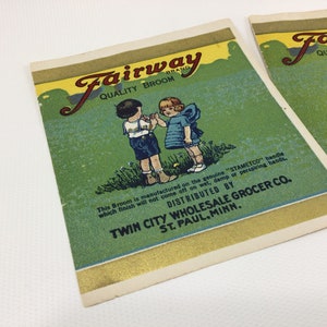 Könnte beinhalten: Vintage-Etikett eines Fairway-Markenbesens mit grünem Hintergrund und zwei Kindern in der Mitte. Das Etikett trägt den Text "Fairway Quality Broom" und "Twin City Wholesale Grocer Co. St. Paul, Minn."