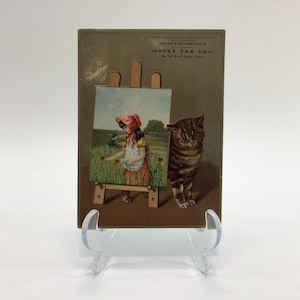 May include: Vintage trade card featuring a girl painting a landscape with a cat watching. The card advertises "Suz Tea Co." and " Teas and Coffees" with the address "No. 121 West Main Street".