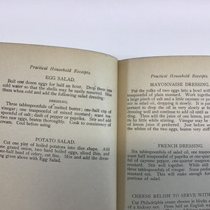 May include: A vintage cookbook with a yellowed, cream-colored paper cover. The book is open to two pages with the titles "Egg Salad", "Potato Salad", "Mayonnaise Dressing", "French Dressing", and "Cheese Relish to Serve with Salad". The text is in black ink and describes how to make each salad.