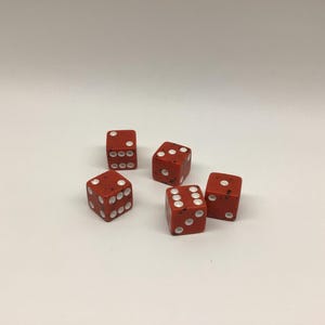 May include: A set of five six-sided dice in a matte red finish with white pips. Each die features rounded corners and a speckled texture across the surface, showing various numerical values including one, three, four, five, and six.