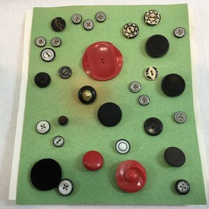 May include: Assortment of vintage buttons in various colors and patterns, including black, white, red, and brown. The buttons are arranged on a green background.