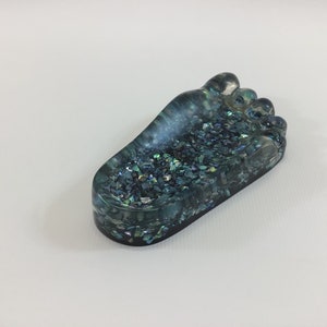 May include: A teal blue resin foot-shaped trinket dish with iridescent glitter embedded in the resin.