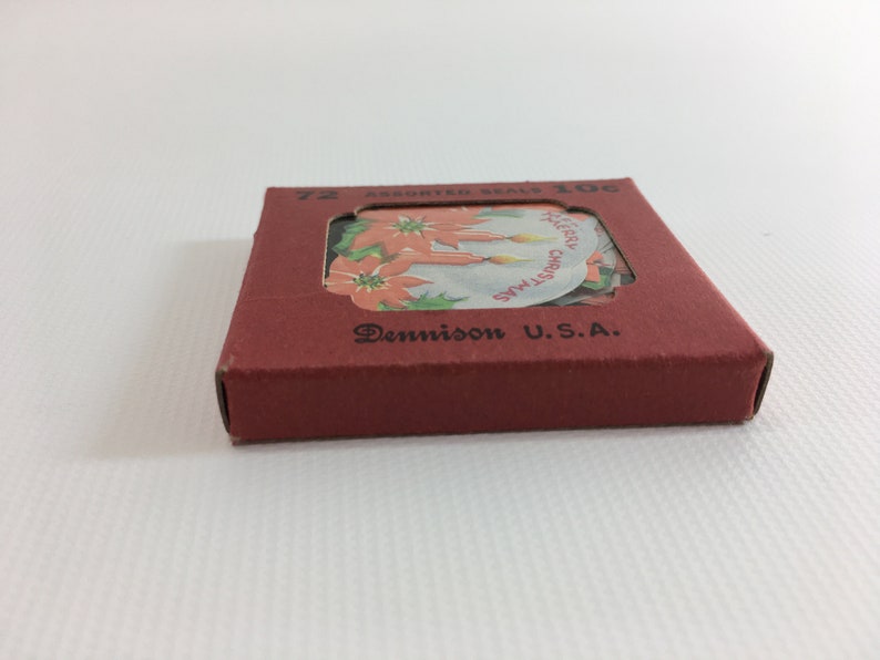K&ouml;nnte beinhalten: Eine rote Schachtel mit einem durchsichtigen Fenster, das eine Bogen mit 72 verschiedenen Weihnachtsbriefmarken zeigt. Die Schachtel tr&auml;gt die Aufschrift "72 Assorted Seals 10c" und "Dennison U.S.A.". Die Briefmarken zeigen einen Weihnachtsstern und Kerzen mit dem Text "Merry Christmas" und "Merry Xmas".