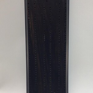 May include: A black wooden cribbage board with a traditional design. The board has multiple rows of holes for pegs.