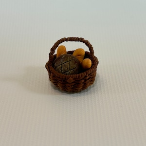 May include: A small brown wicker basket filled with bread. The basket has a woven handle and contains a round loaf of bread and two smaller loaves.