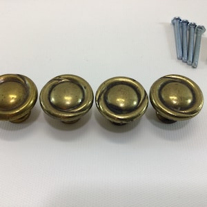 May include: Four gold-toned cabinet knobs with a decorative swirl design. The knobs are round and have a slightly raised center.