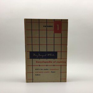 May include: A hardcover book titled Mary Margaret McBride Encyclopedia of cooking Volume 1. The cover is tan with a black and red grid pattern. It features the text ABC's for cooks, Appetizers and party snacks, and Bean bakes in red and black.