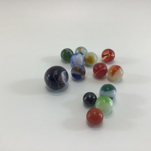 May include: A collection of colorful glass marbles in various shades of red, blue, green, and white. The marbles are arranged in a loose cluster on a white surface.