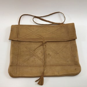 May include: A tan leather satchel bag with a flap closure and a braided strap. The bag has a decorative embossed pattern and a tassel.