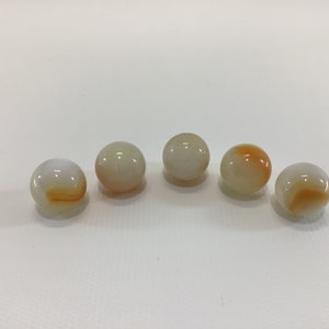 May include: Five white agate marbles with orange and brown swirls. The marbles are arranged in a semi-circle on a white surface.