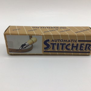 May include: A brown cardboard box with the words "Automatic Stitcher" printed in blue and white. The box shows a close-up of the stitching tool in use on a brown leather belt. The box also lists the uses for the tool: belts, shoes, handbags, luggage, and upholstery.