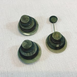 May include: A set of three green and black layered circle earrings. The earrings are made of a layered material that resembles wood or plastic.