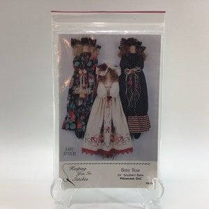 May include: A sewing pattern for a 24-inch Southern Belle pillowcase doll. The pattern is called "Betsy Rose" and is from the "Keeping You In Stitches" line. The pattern shows three dolls in different dresses, one with a red, white, and blue dress, one with a white dress, and one with a floral dress.