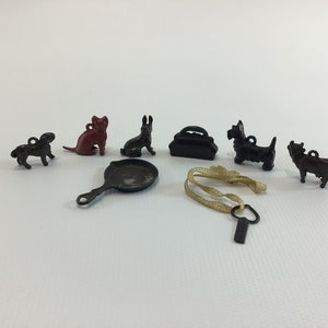 May include: A set of miniature metal figurines, including a cat, rabbit, two dogs, a cow, a small suitcase, and a frying pan. The figurines are black, red, and brown.