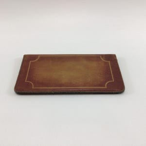 May include: A brown leather wallet with a gold border around the edges.